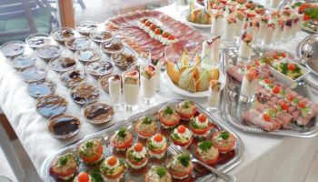 Ein Tisch mit einer Vielzahl von Vorspeisen, darunter Salate, Sandwiches und Dips, auf Silberschalen und Schüsseln angeordnet.