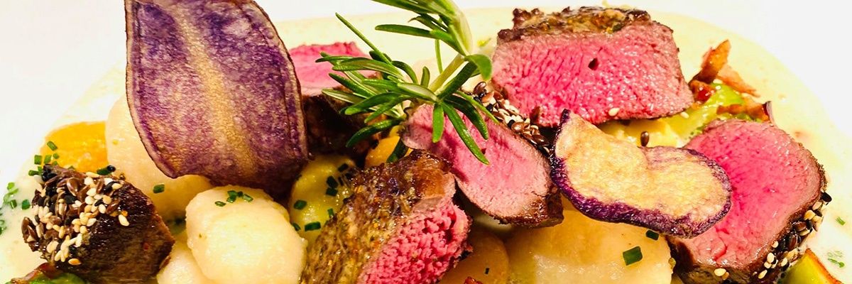 Eine Nahaufnahme eines Tellers mit Steakscheiben, lila Kartoffeln und gelben Kartoffeln, garniert mit Rosmarin.