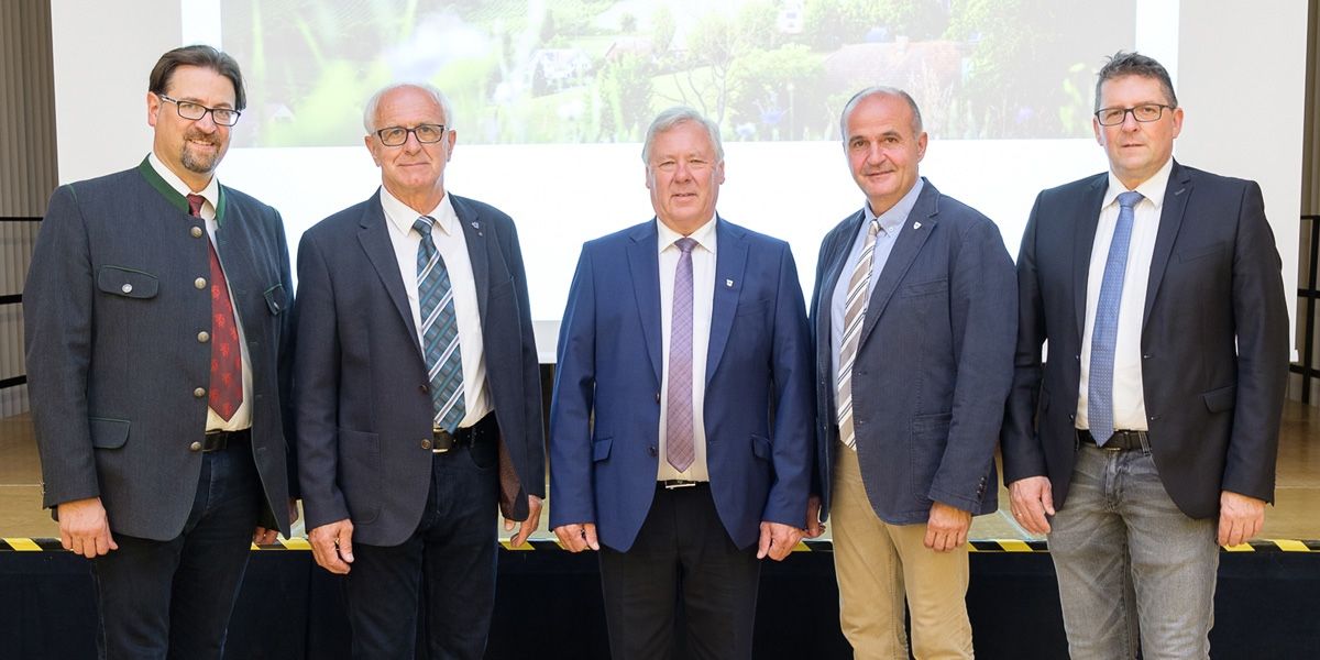 Fünf Männer in Anzügen und Krawatten stehen vor einer Leinwand, die eine Landschaft zeigt.