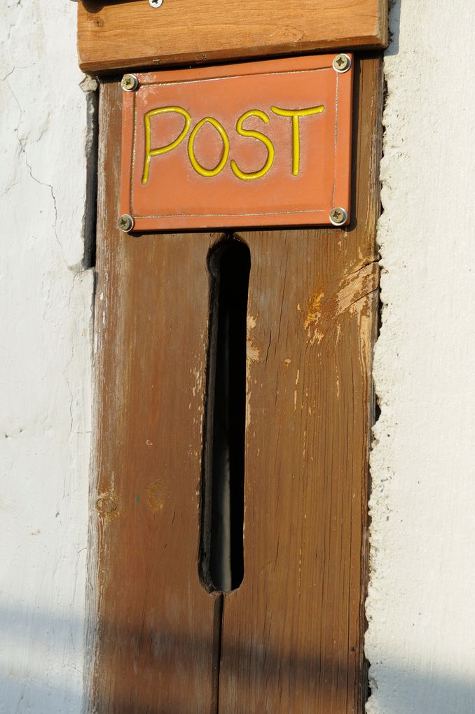  Abschnitt Bild: Ein hölzerner Briefschlitz mit einem Schild, das POST beschriftet ist. Die hölzerne Oberfläche zeigt Abnutzungsspuren und eine Risse an der Wand.