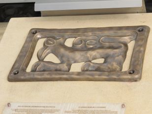 Ein ausgestelltes bronzenes Relief zeigt ein stilisiertes Tier. Darunter befindet sich Text. Das Objekt scheint ein historisches Artefakt zu sein.
