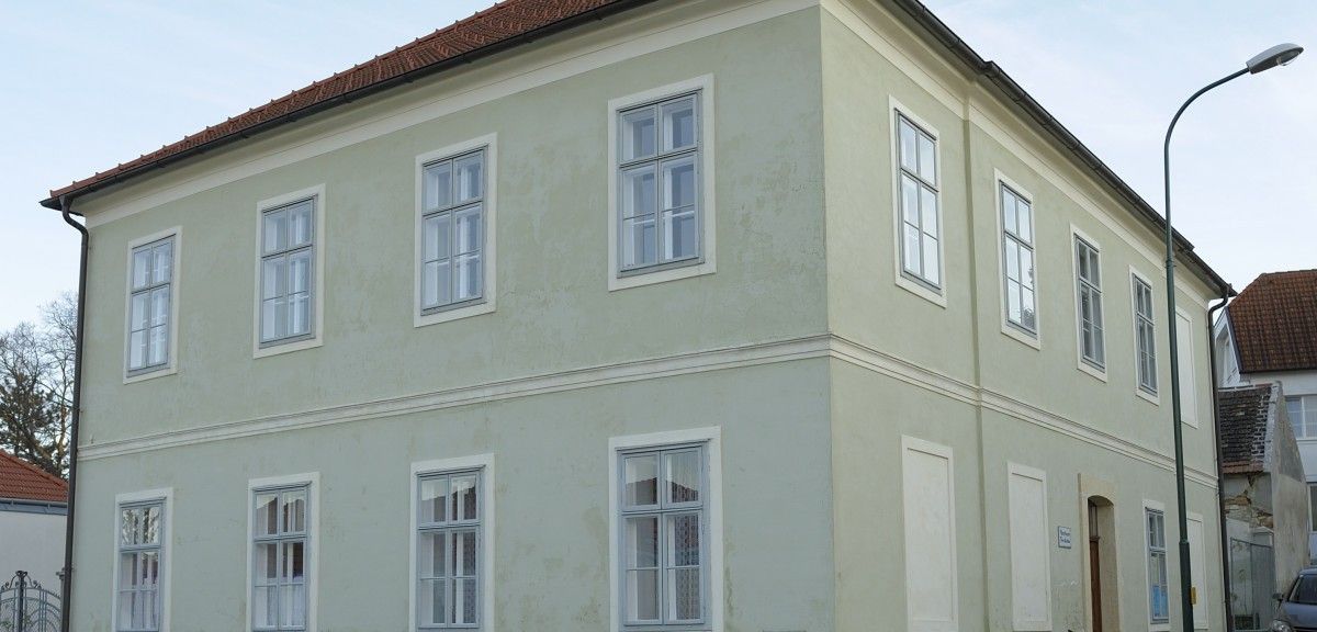 Ein hellgrünes Gebäude mit einem roten Dach und mehreren Fenstern an der Vorderseite.