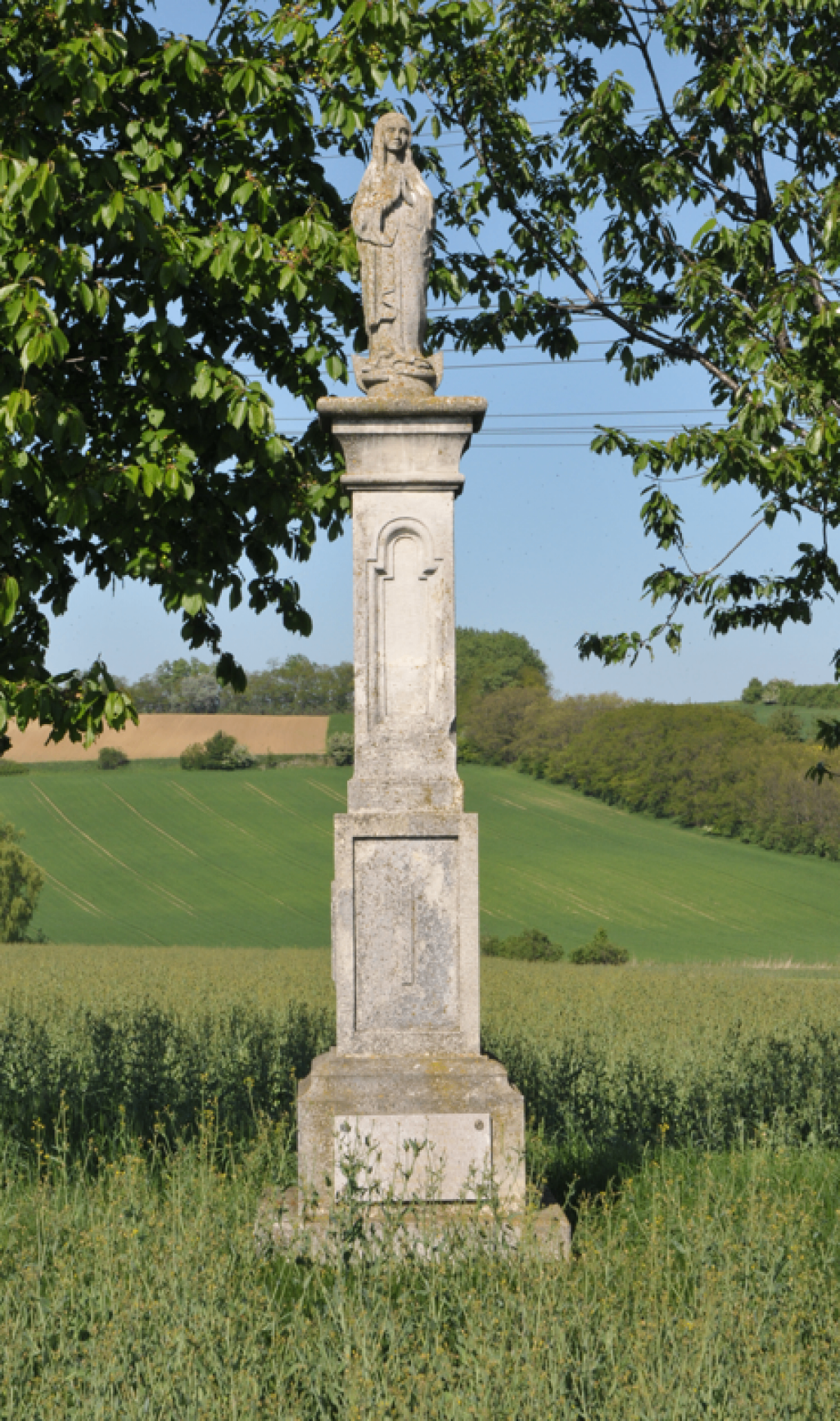 Ein altes Steinmonument steht in einem grünen Feld unter einem Baum, umgeben von einer grünen Landschaft.