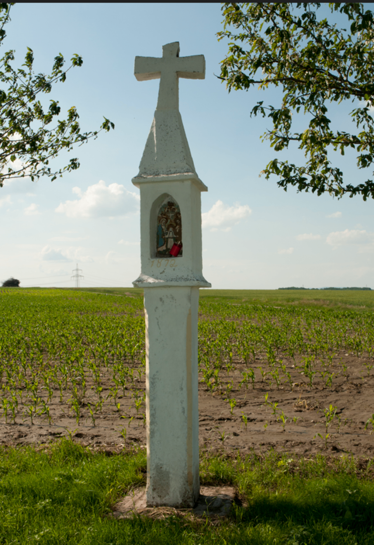Eine kleine weiße Kapelle auf einem grünen Feld mit einem roten Vorhängeschloss und einem Bild von Jesus Christus.