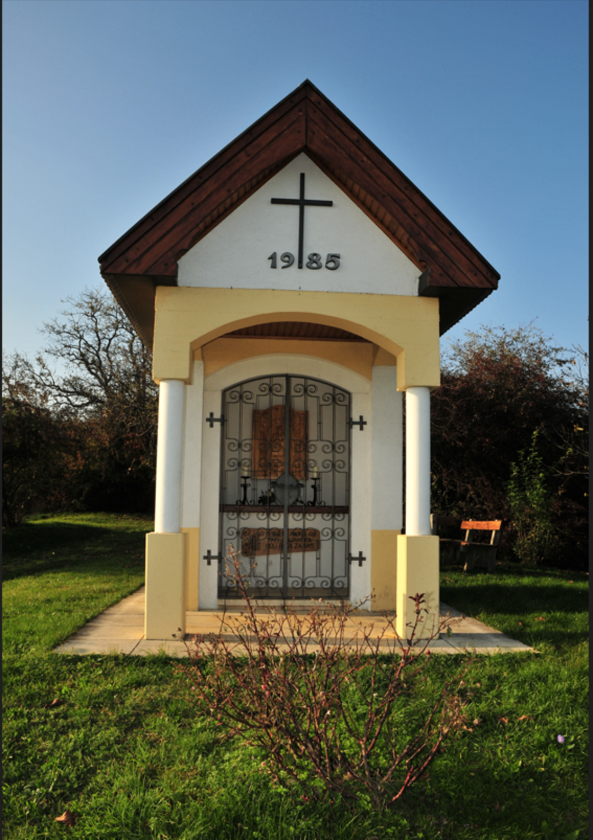 Eine kleine Kapelle mit einem Kreuz auf dem Dach, der Nummer 19185 darunter und einer geschlossenen Metalltür mit einem Kreuz darauf.