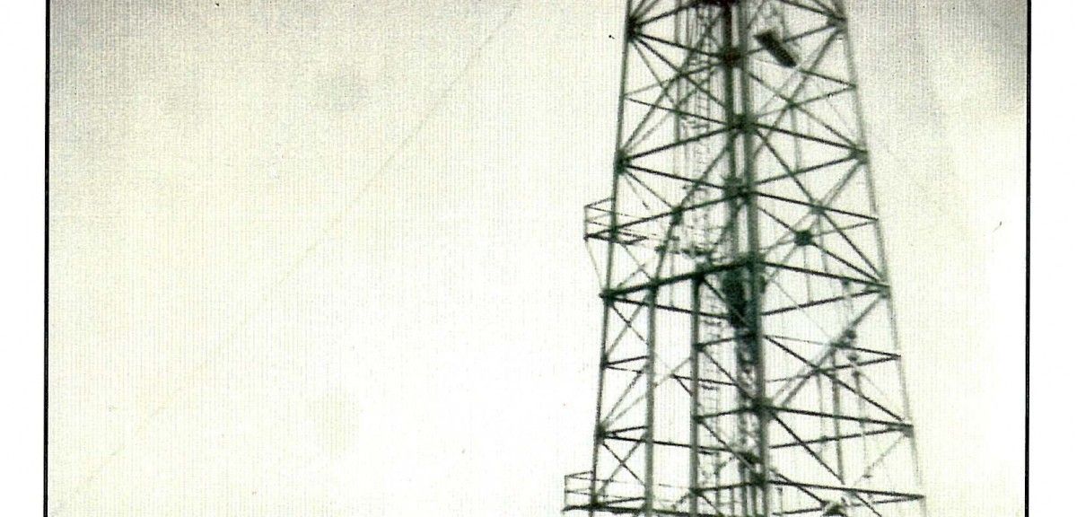 Eine hohe Metallstruktur mit einer Leiter und verschiedenen Ebenen, möglicherweise ein Funkturm. Das Bild ist in Schwarz-Weiß gehalten.