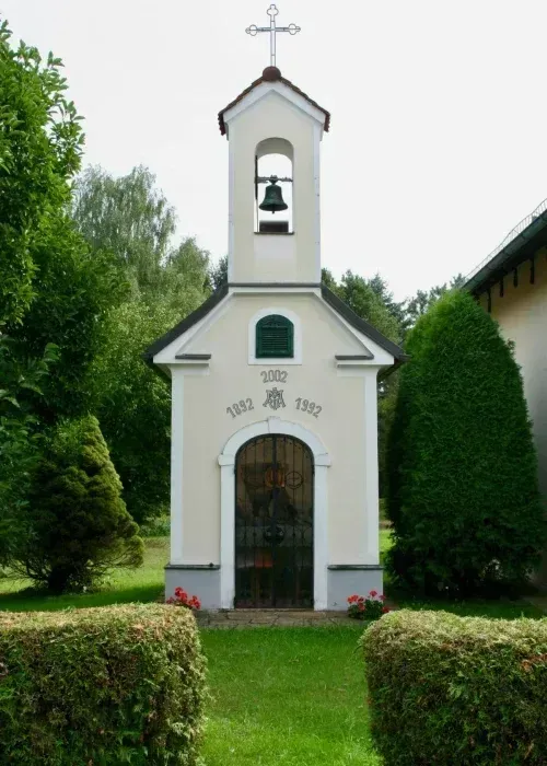 Eine kleine weiße Kirche mit Glockenturm und Glocke. Die Jahre 1832 und 1992 sind in die Wand graviert.