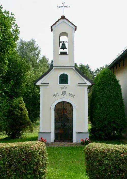 Eine kleine weiße Kirche mit Glockenturm und Glocke. Die Jahre 1832 und 1992 sind in die Wand graviert.