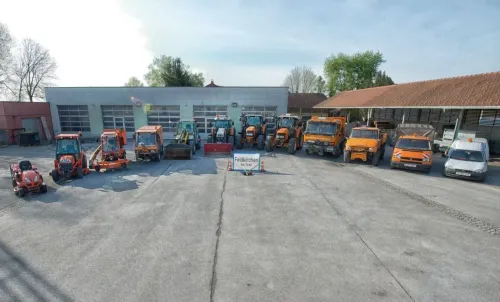 Mehrere orangefarbene Maschinenfahrzeuge sind in einer Reihe vor einem Gebäude geparkt, an dem ein Schild mit der Aufschrift Feldkirchen steht.
