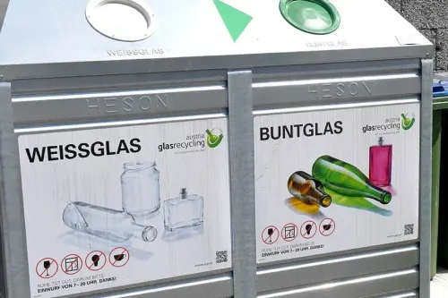 Zwei Recyclingbehälter für farbiges und klares Glas mit einem glassrecycling Austria Logo. Ein Schild mit Symbolen und einer Nachricht in Deutsch.