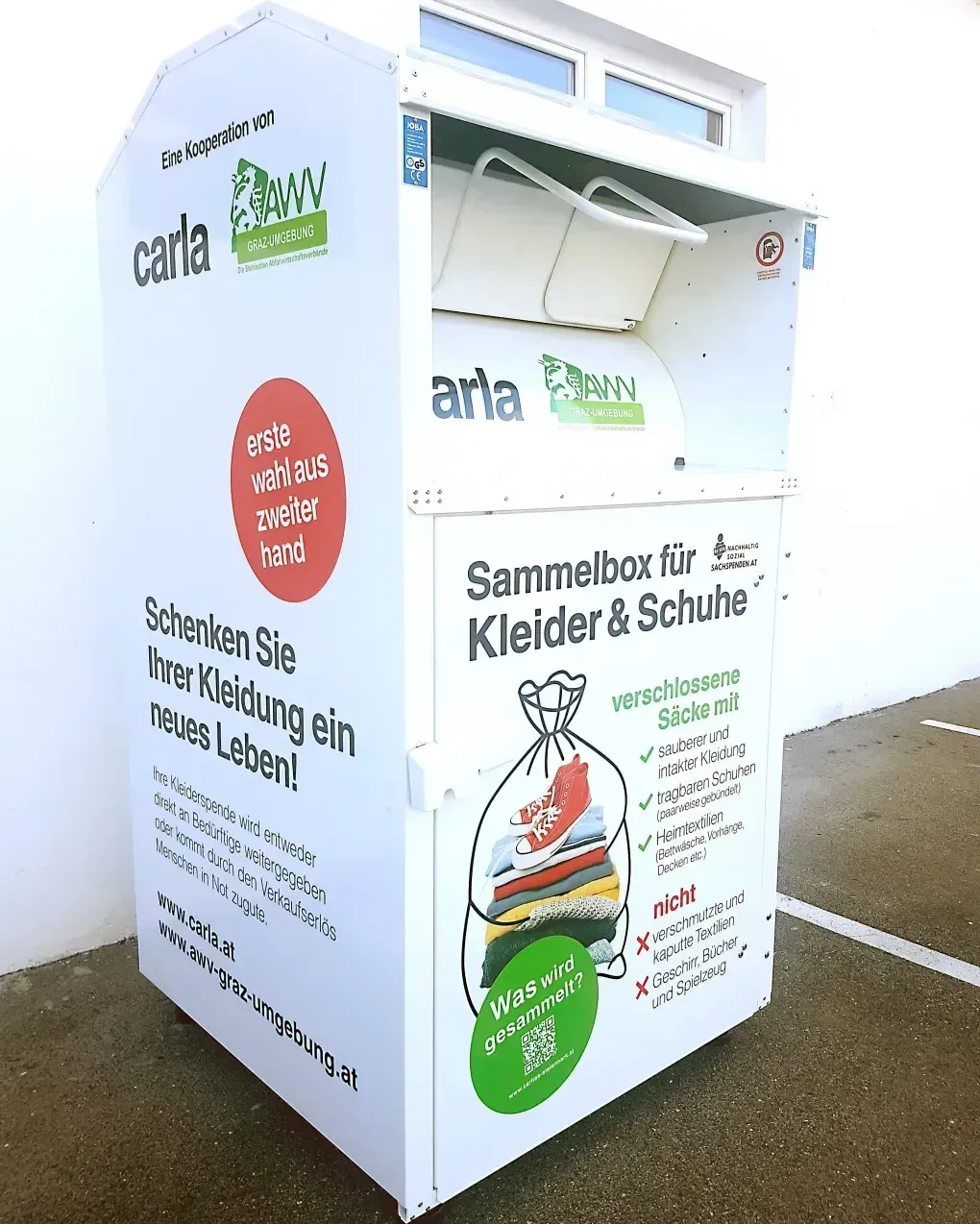 Ein weißer Spendenbox für Kleidung und Schuhe mit einem offenen Beutel. Es steht 'Schenken Sie Ihre Kleidung ein neues Leben' und wird von Carl AWV gesponsert.