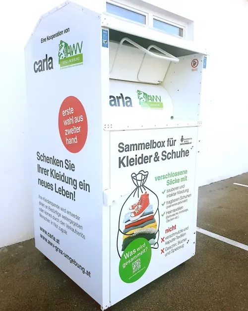 Ein weißer Spendenbox für Kleidung und Schuhe mit einem offenen Beutel. Es steht 'Schenken Sie Ihre Kleidung ein neues Leben' und wird von Carl AWV gesponsert.