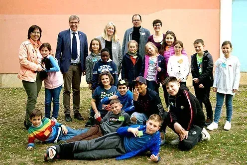 Eine Gruppe von Erwachsenen und Kindern posiert für ein Foto vor einer bunten Wand, wobei einige der Kinder Namensschilder tragen.