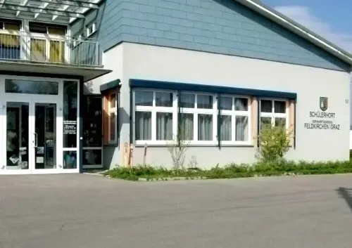 Ein modernes Gebäude mit Glastüren und Fenstern trägt ein Schild mit der Aufschrift Schulerhof Gemeinschaftsschule Feldkirchen/Graz.