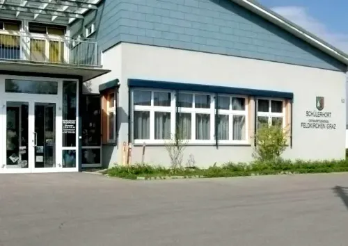Ein modernes Gebäude mit Glastüren und Fenstern trägt ein Schild mit der Aufschrift Schulerhof Gemeinschaftsschule Feldkirchen/Graz.