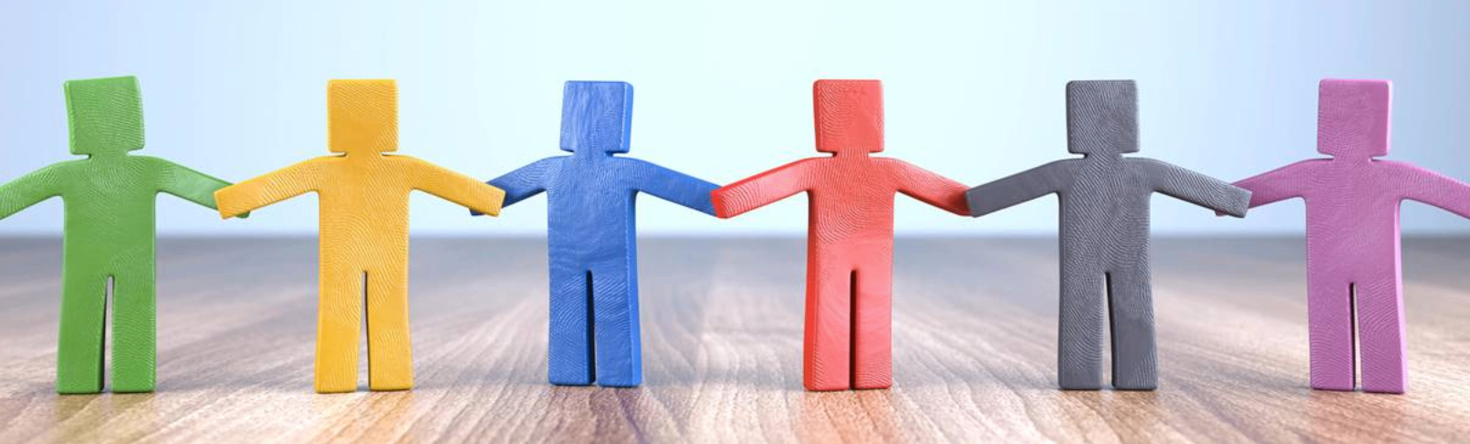 Vier hölzerne Figuren in verschiedenen Farben halten Händchen. Sie sind gelb, blau, rot und grau. Der Hintergrund ist blau.