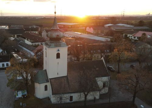 Eine Draufsicht auf eine Kirche mit Turm und Uhrenturm bei Sonnenuntergang, umgeben von Bäumen und Gebäuden.
