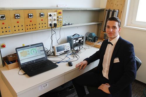 Ein Mann in Anzug und Fliege sitzt an einem Schreibtisch mit Laptop, Maus und verschiedenen elektronischen Geräten.