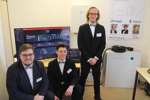 Drei Männer in Anzügen und Fliegen posieren für ein Foto mit einem großen Monitor, einem Laptop und einem weißen Netzteil.