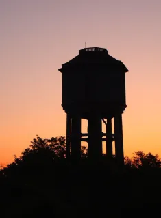 Eine Silhouette eines Wasserturms steht gegen den Sonnenuntergang, umgeben von Bäumen.