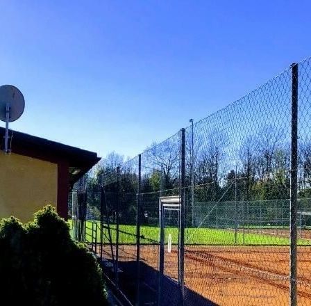 Ein Tennisplatz mit einem Gebäude, auf dem Askó T.C. Hirm steht. Das Gebäude hat einen Basketballkorb an der Wand montiert.