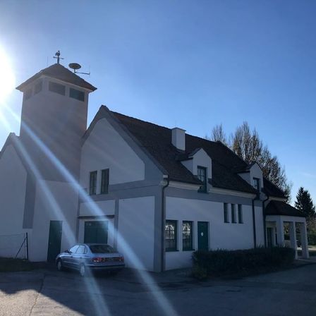 Das weiße Gebäude mit schwarzem Dach und Turm ist eine Kirche. Vor dem Gebäude ist ein Auto geparkt.