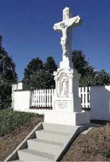 Ein weißes Kreuzmonument steht auf einem Friedhof, mit einer Statue von Jesus Christus am Kreuz und einem weißen Lattenzaun dahinter.
