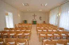 Eine leere Kapelle mit Holzstühlen und einem Kreuz an der Wand.