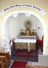 Ein Altar in einer Kirche mit einer Statue der Maria und einem Banner darüber.