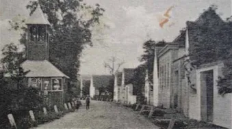 Ein altes Schwarz-Weiß-Foto einer Straße mit einer Kirche auf der linken Seite und Häusern auf der rechten Seite. Eine Person geht die Straße entlang.