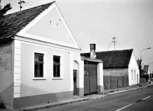 Ein Schwarz-Weiß-Foto eines kleinen Hauses mit Schornstein und zwei Fenstern.