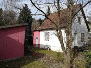 Ein altes weißes Haus mit einem roten Dach und einer roten Wand auf der linken Seite.