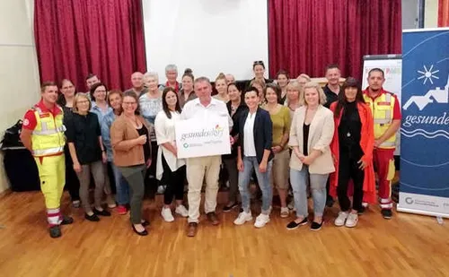Eine Gruppe von Menschen in verschiedenen Outfits posiert für ein Foto in einem Raum, ein Mann hält ein großes weißes Zertifikat.