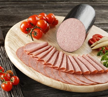 Ein Holzschneidebrett hat geschnittenen Salami, geschnittene Kirschtomaten und Petersilie. Der Salami ist in der Mitte, und die geschnittenen Tomaten sind auf beiden Seiten.