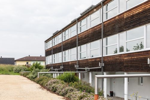 Ein modernes Gebäude mit Holzfassade und Glasfenstern, neben einem Garten mit blühenden Blumen.