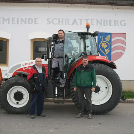 Drei Männer stehen vor einem roten und weißen Traktor. Ein Mann steht im Fahrersitz des Traktors.