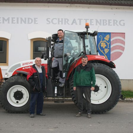 Drei Männer stehen vor einem roten und weißen Traktor. Ein Mann steht im Fahrersitz des Traktors.