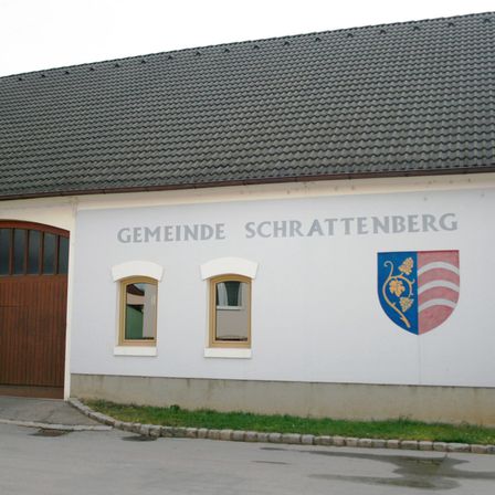 Außenansicht eines weißen Gebäudes mit dem Text Gemeinde Schrattenberg und einem Wappen an der Wand.