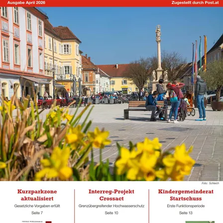Ein Stadtplatz mit Menschen, einem Denkmal und geparkten Fahrrädern. Gebäude mit Vordächern und geparkten Autos. Das Bild ist vom April 2026 und zeigt eine aktualisierte Kurzparkzone.