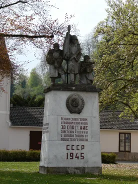 Ein weißes Denkmal mit einer Tafel und drei Statuen von Soldaten, die Gewehre halten. Es steht 'Für die Sowjetarmee', '1945' und 'Für die Befreiung der Sowjetunion und der europäischen Völker vom Faschismus.'