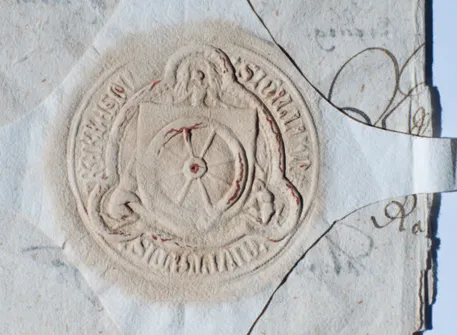 Ein verwitterter, strukturierter Siegelabdruck mit einem kreisförmigen Design, das ein Rad, einen Engel und Text am Rand zeigt, auf einem Papierfragment geprägt.