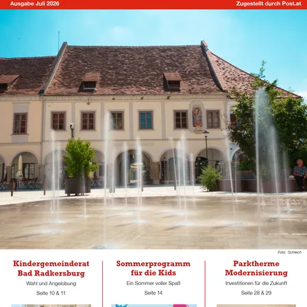 Ein Brunnen vor einem historischen Gebäude mit einem Ziegeldach und mehreren Fenstern. Das Gebäude hat eine Statue über dem Eingang. Im Vordergrund befinden sich Bäume und Pflanzen.