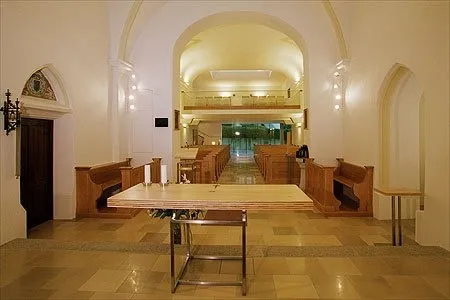Innenansicht einer Kirche mit einem langen Tisch in der Mitte, hölzernen Bänken auf beiden Seiten und einer Tür auf der linken Seite.