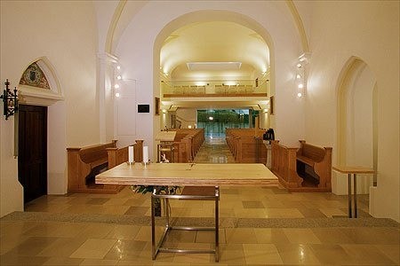 Innenansicht einer Kirche mit einem langen Tisch in der Mitte, hölzernen Bänken auf beiden Seiten und einer Tür auf der linken Seite.