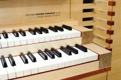 Nahaufnahme eines Klaviers mit zwei Tastenreihen, die obere Reihe hat schwarze Tasten und die untere Reihe hat weiße Tasten. Das Klavier hat ein Holzgehäuse und Metallakzente.