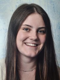 Eine Frau mit langen braunen Haaren und einer Halskette lächelt in die Kamera.