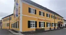 Ein gelbes Gebäude mit schwarzen Fensterläden steht an der Straßenseite. Das Gebäude hat ein Schild auf der Spitze, das "Zimmer" steht. Das Gebäude ist gelb gestrichen mit weißen Verkleidungen.