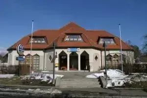 Ein großes weißes Gebäude mit einem roten Dach und Bogenfenstern, umgeben von Schnee, mit zwei Stangen davor und einem klaren blauen Himmel.