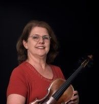 Eine Frau mit Brille und rotem Shirt lächelt und hält eine Geige.