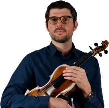 Ein Mann in einem blauen Hemd und mit Brille hält eine Geige mit einem Bogen in den Händen.